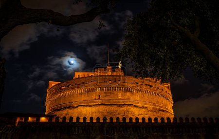 Téléchargez les photos : Vue de nuit à travers les branches d'un arbre de la forteresse de Castel Sant'Angelo à Rome - en image libre de droit