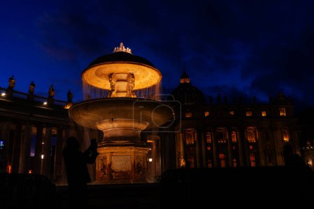 Téléchargez les photos : Image nocturne d'un touriste photographiant l'une des fontaines illuminées de la place Saint-Pierre Rome - en image libre de droit