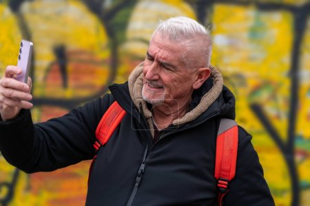 Téléchargez les photos : Heureux homme d'âge moyen en vacances prendre un selfie en face de graffitis déconcentrés à Rome - concept amusant et vacances. - en image libre de droit