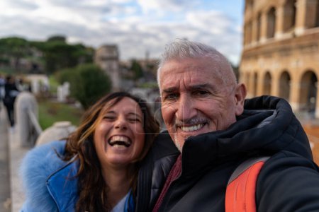 Téléchargez les photos : Heureux couple d'âge moyen en vacances prendre un selfie en face de l'amphithéâtre Colisée à Rome - concept amusant et vacances. - en image libre de droit