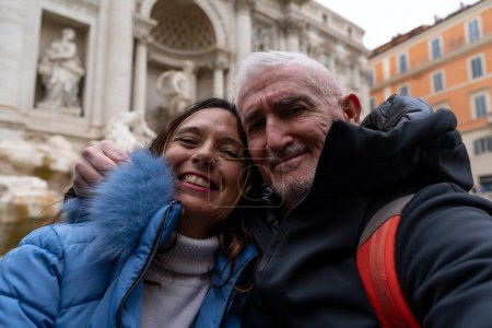 Foto de Feliz pareja de mediana edad de vacaciones tomando una selfie frente a una famosa fuente de Trevi en Roma - diversión y concepto de vacaciones. - Imagen libre de derechos