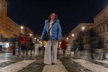 Photo for Female tourist posing among blurry people walking at night on a street in front of the vatican in rome - travel concept - Royalty Free Image