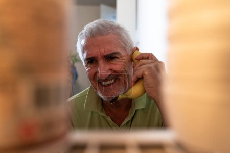 Photo for Middle aged single man having fun using a banana as a phone in front of the refrigerator - view from inside the home appliance - Royalty Free Image