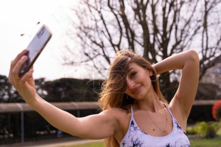 Téléchargez les photos : Jeune femme sportive blonde charmante en vêtements de sport posant prendre un selfie à l'extérieur concept de vie saine - en image libre de droit