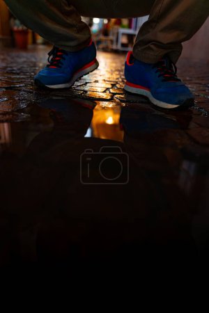 Photo for Male feet in blue sneakers are reflected in a puddle of a city street in the evening - Royalty Free Image