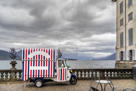 Foto de Vehículo motorizado de tres ruedas para la venta de helados estacionado en la terraza del palacio Borromeo en Isola Bella - vista panorámica del lago Maggiore - Imagen libre de derechos
