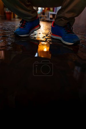 Foto de Pies masculinos en zapatillas azules se reflejan en un charco de una calle de la ciudad por la noche - Imagen libre de derechos