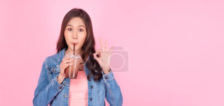 Photo for Cheerful asian woman drink ice cocoa with straw thirsty refreshment  looking camera on pink background. Portrait excited girl holding ice beverage in cup plastic use straw drinking relax over isolated - Royalty Free Image