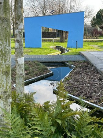 Téléchargez les photos : Appeltern, Pays-Bas, 09 avril 2023 : Terrasse moderne d'avant-garde avec un mur bleu et une arche, un étang et des sentiers en béton sur une pelouse. Plantes : fougère dryopteris erythrosora, bouleau himalayen doorenbos - en image libre de droit