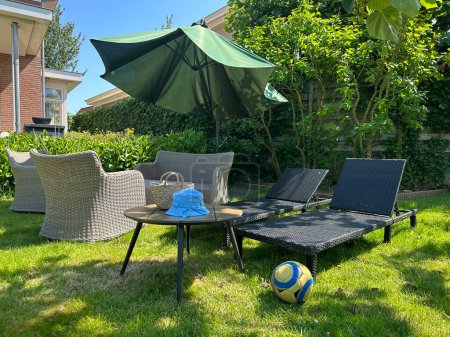 Foto de Jardín de verano con césped verde, silla de mimbre y sombrilla. Acogedora zona de estar - Imagen libre de derechos