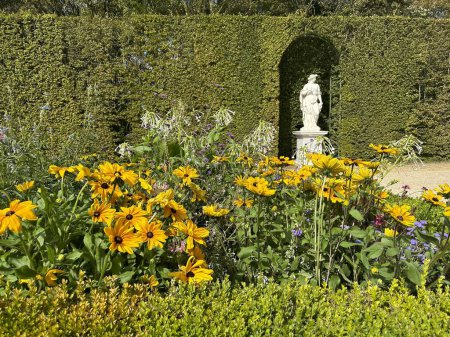 Foto de Versalles, Francia, 12 de agosto de 2023: Parque de Versalles. Flores perennes y setos con escultura en el jardín del palacio de Versalles - Imagen libre de derechos