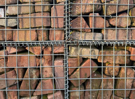 Fragment of grey metal wire fence filled with bricks
