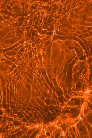 Téléchargez les photos : Défocus flou transparent orange clair texture de surface de l'eau calme avec éclaboussures et bulles. Fond nature abstrait à la mode. Ondes d'eau au soleil avec espace de copie. Eau orange brillante - en image libre de droit