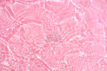 Foto de Desenfoque borroso transparente de color rosa claro textura de la superficie del agua calma con salpicaduras y burbujas. Fondo de naturaleza abstracta de moda. Ondas de agua a la luz del sol con espacio para copiar. Acuarela rosa brillante - Imagen libre de derechos