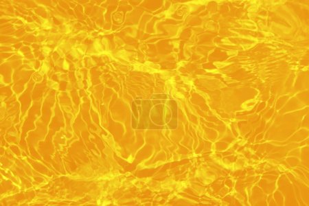 Foto de Desenfoque borrosa transparente de color naranja claro textura de la superficie del agua calma con salpicaduras y burbujas. Fondo de naturaleza abstracta de moda. Onda de agua a la luz del sol con espacio para copiar. Color naranja gota de agua - Imagen libre de derechos