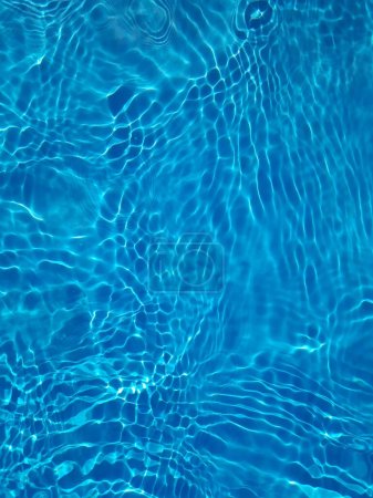 Foto de Desenfoque borrosa transparente de color azul claro textura de la superficie del agua calma con salpicaduras y burbujas. Fondo de naturaleza abstracta de moda. Ondas de agua a la luz del sol con cáusticos. Brillo de agua azul - Imagen libre de derechos