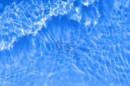 Defocus blurred transparent blue colored clear calm water surface texture with splashes and bubbles. Trendy abstract nature background. Water waves in sunlight with caustics. Blue water shinning 
