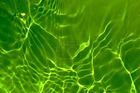 Defocus verschwommen transparent grün gefärbt klare ruhige Wasseroberfläche Textur mit Spritzer, Blase. Leuchtend grünes Wasser plätschert vor sich hin. Wasseroberfläche im Schwimmbad. Tropisch grüne Wassertexturen.