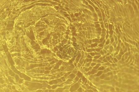 Téléchargez les photos : Defocus blurred transparent gold colored clear calm water surface texture with splashes and bubbles. Trendy abstract nature background. Water waves in sunlight with caustics. Yellow water shinning - en image libre de droit