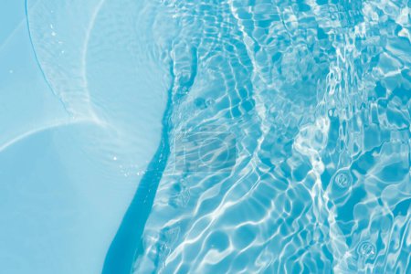 Ondes d'eau bleue sur les ondulations de surface floues. Défocus flou transparent bleu clair texture de surface de l'eau calme avec éclaboussures et bulles. vagues d'eau avec motif brillant texture fond.