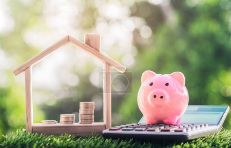 Photo for Coins placed in a model house and a piggy banks on the calculator on the grass. planning savings money of coins to buy a home concept for property, mortgage and real estate invest, savings for a house - Royalty Free Image