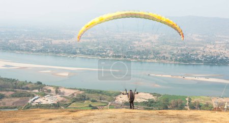 Photo for Paragliding in the sky. Paraglider  flying over Landscape from Beautiful View Mekong River at Wat Pha Tak Suea in Nongkhai, Thailand.Aerial view. Concept of extreme sport, taking adventure/ challenge. - Royalty Free Image