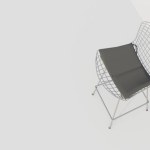 A white chair with a black cushion sits on a white wall. The chair is made of metal and has a mesh design. The chair appears to be modern and sleek, with a minimalist design