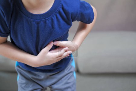 Foto de Un niño con dolor en el estómago se frota el estómago en el punto de dolor - Imagen libre de derechos