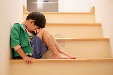 Foto de Un triste chico asiático se sienta con la cabeza abajo en las escaleras - Imagen libre de derechos