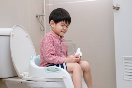Photo for Asian boy Sitting on the toilet bowl in hand holding tissue - Royalty Free Image