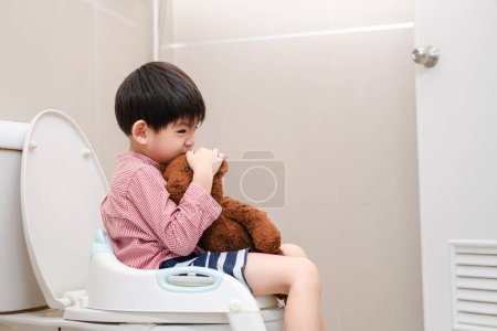 Foto de Asiático chico sentado en el inodoro en mano sosteniendo osito de peluche - Imagen libre de derechos