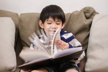 Foto de Asiático chico leyendo un libro en el sofá aprendiendo fuera del aula - Imagen libre de derechos