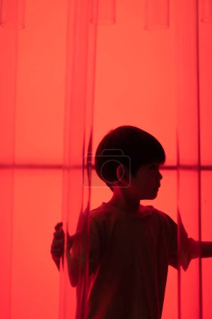 Little Asian boy, dark red background.