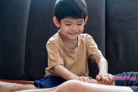 A young Asian child is taking care of his mother by massaging her muscles to relax her.
