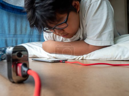Photo for An Asian boy lies prone while seeing media on a smartphone - Royalty Free Image