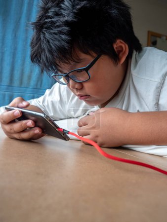 Photo for An Asian boy lies prone while seeing media on a smartphone - Royalty Free Image