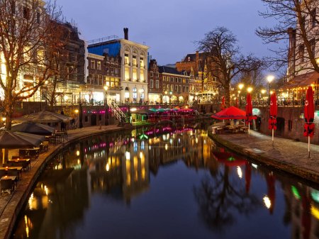 Beautiful canals cityscape under warm lights during a misty and cloudy winter evening, Utrecht, Netherlands