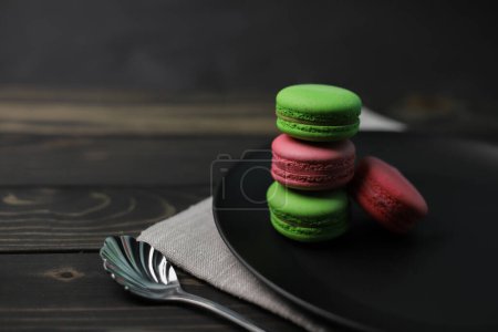 Photo for Traditional American macaroons in pink and bright green color on a wooden background and a black plate next to purple fragrant flowers - Royalty Free Image