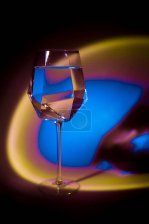 verre transparent avec de l'eau en néon saturé de couleurs arc-en-ciel lumineuses psychédéliques