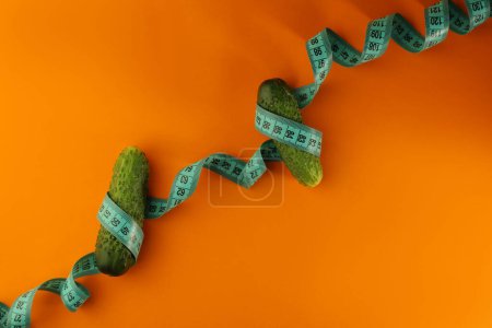 on a bright orange background, a blue sewing centimeter and various healthy vegetables arugula cucumbers lemon. for banners, intros, advertising labels and more