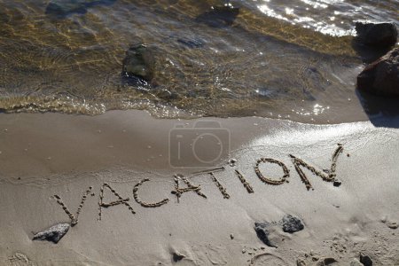 Photo for The inscription word vacation on a wet sandy shore with stones on the beach by the river and the sun is reflected in the glare in the water - Royalty Free Image