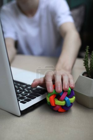 Téléchargez les photos : Photo where a guy who works and studies online on a white laptop in a white t-shirt and relieves stress during a break with a rubber ball of bright color to relieve stress - en image libre de droit