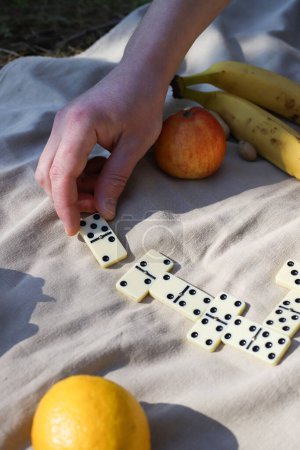 game of dominoes at a picnic. leisure. There is a domino on the picnic mat and nearby there are nuts, apples, water and bananas for a healthy snack.