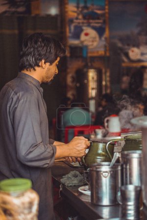 Pakistani man food vendor preparing smoking hot masala chai, the local tea, in a kettle in his roadside street food stall