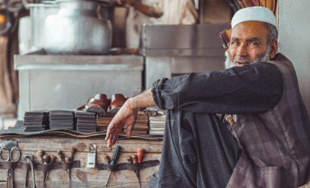 Pobre viejo y triste zapatero pakistaní Pathan en las calles locales de Pakistán con sus zapatos de cuero hechos a mano y herramientas de reparación en su tienda de la calle