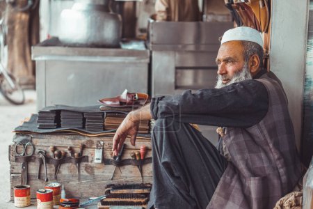 Pobre zapatero pathan paquistaní viejo zapatero en las calles locales de Pakistán con sus zapatos de cuero hechos a mano y herramientas de reparación en su tienda de la calle