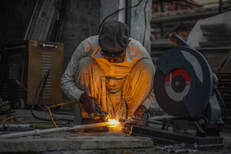 Pobre viejo y experto soldador paquistaní tubos de soldadura y varillas de metal en su taller de la calle