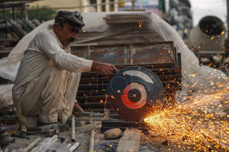 Pobre viejo soldador paquistaní cortando tuberías y varillas de metal en su taller callejero con cortador eléctrico causando llamas y chispas