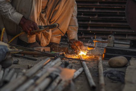 Soldador tubos de soldadura y varillas de metal en su taller de la calle causando chispas y llamas