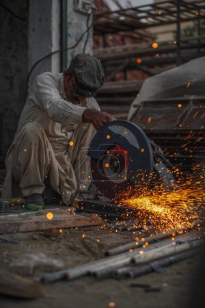 Photo for Poor old Pakistani Welder cutting pipes and metal rods in his street workshop with electric cutter causing flames and sparks - Royalty Free Image
